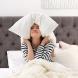 Une jeune femme qui se bouche les oreilles avec un oreiller dans son lit