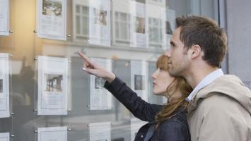 couple devant une vitrine d'annonces immobilières