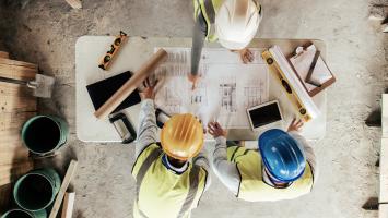 Trois ouvriers en gilets  et casques discutent des plans architecturaux sur un chantier