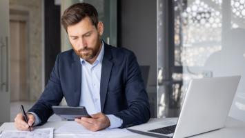 Un homme d'affaires consulte son téléphone et des documents dans un bureau moderne.