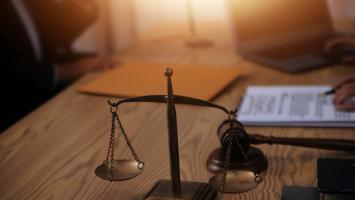  Une balance de la justice en premier plan sur un bureau avec des personnes travaillant en arrière-plan.
