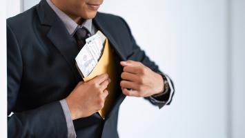  Un homme en costume insère discrètement une enveloppe contenant des billets de banque dans sa veste.