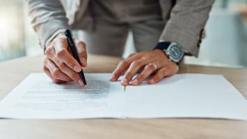 Un homme signe des documents officiels sur un bureau.