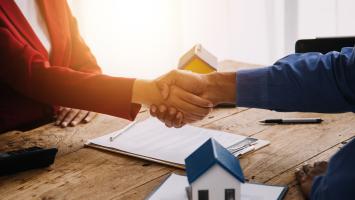  Deux personnes se serrent la main lors d'un accord, avec une maquette de maison et des documents sur la table