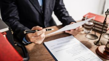 Avocat examinant un document contractuel avec un stylo à la main.