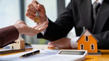 Un agent immobilier remet les clés d'une maison à un nouveau propriétaire, symbolisé par une maquette de maison et un contrat sur une table