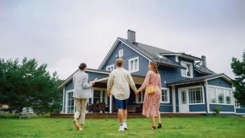Un couple visite une maison avec une agente immobilière, située dans un cadre verdoyant.