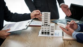 Un homme d'affaires professionnel en costume tient une réunion au bureau tout en présentant un modèle d'immeuble en copropriété