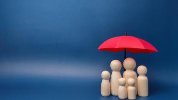Une famille de petits bonhommes en bois abritée sous un parapluie rouge