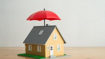 Une maison modélisée protégée par un parapluie ouvert de couleur rouge