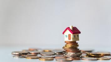 Une maison miniature au toit rouge posée sur un tas de pièces de monnaie