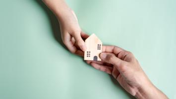 Une maison miniature en bois portée par deux mains