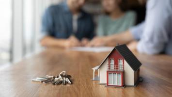 Une maison miniature posée à côté de clés avec des locataires en arrière-plan 