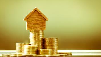 Une maison miniature en bois posée sur une pile de pièces de monnaie dorées