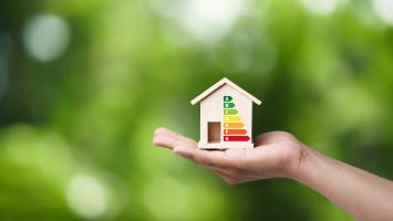 Le DPE inscrit sur une maison miniature en bois posée sur une main