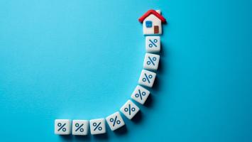 Des dés en forme de pourcentage alignés en courbe vers une petite maison, sur fond bleu turquoise