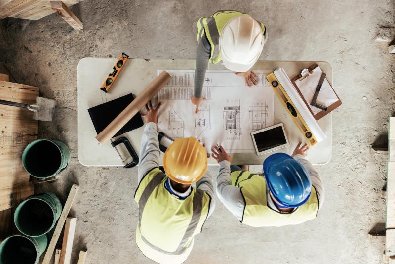 Trois ouvriers en gilets  et casques discutent des plans architecturaux sur un chantier