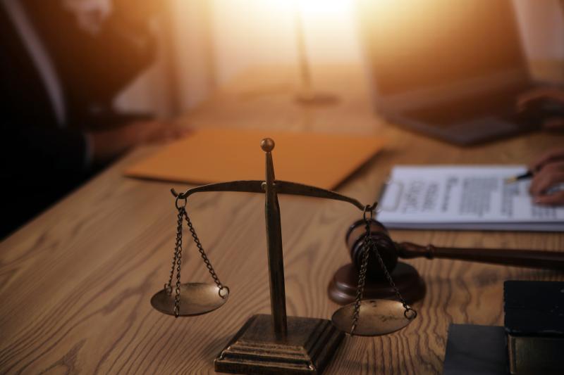  Une balance de la justice en premier plan sur un bureau avec des personnes travaillant en arrière-plan.