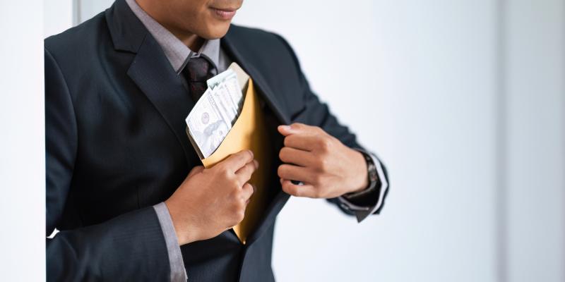  Un homme en costume insère discrètement une enveloppe contenant des billets de banque dans sa veste.