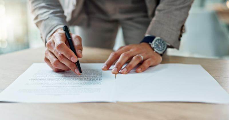 Un homme signe des documents officiels sur un bureau.