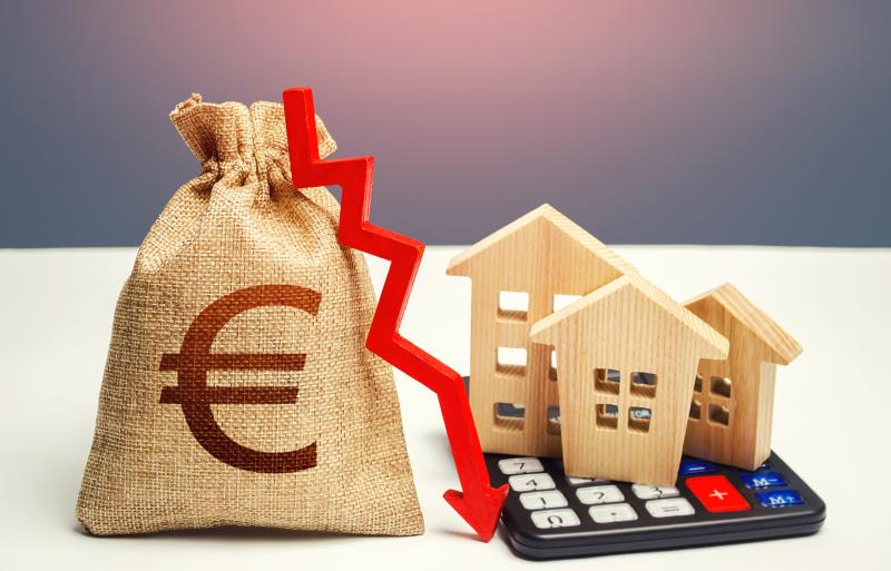 Un sac d'argent avec un symbole euro, une flèche rouge pointant vers le bas, des maisons en bois et une calculatrice, symbolisant la diminution de la valeur immobilière.