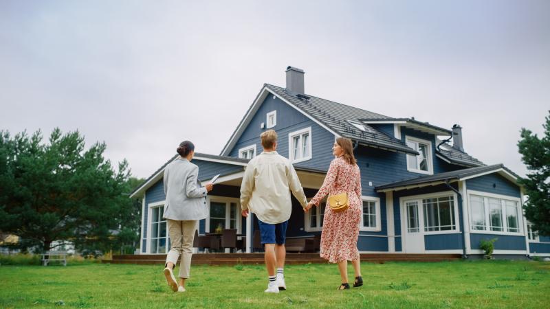 Un couple visite une maison avec une agente immobilière, située dans un cadre verdoyant.