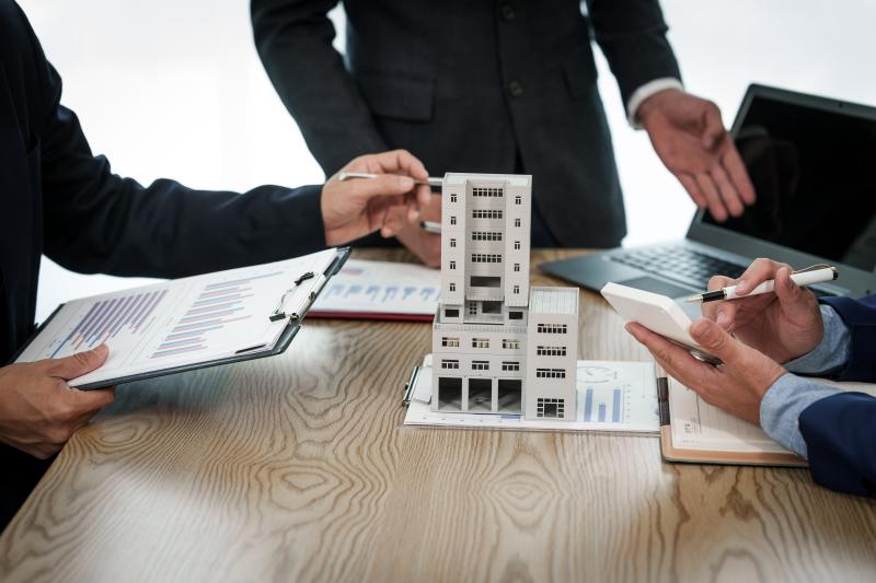 Un homme d'affaires professionnel en costume tient une réunion au bureau tout en présentant un modèle d'immeuble en copropriété