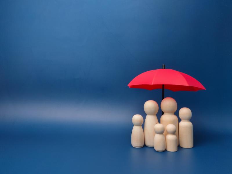 Une famille de petits bonhommes en bois abritée sous un parapluie rouge