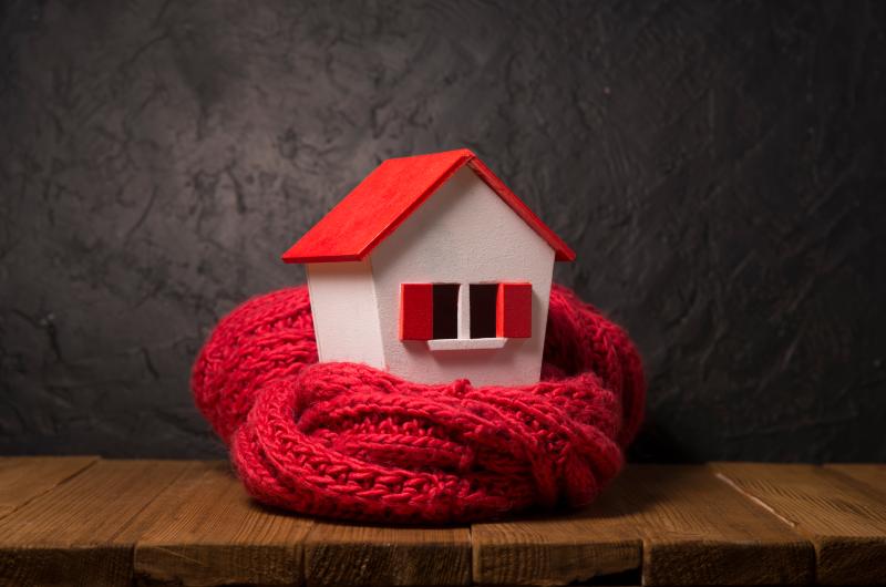 Une maison miniature entourée d'une écharpe en laine rouge