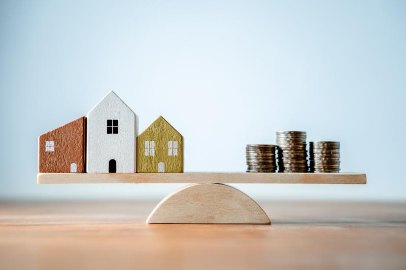 Des maisons et des pièces de monnaie en équilibre sur une planche de bois