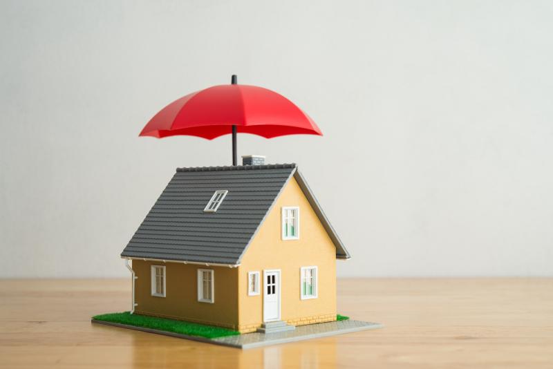 Une maison modélisée protégée par un parapluie ouvert de couleur rouge