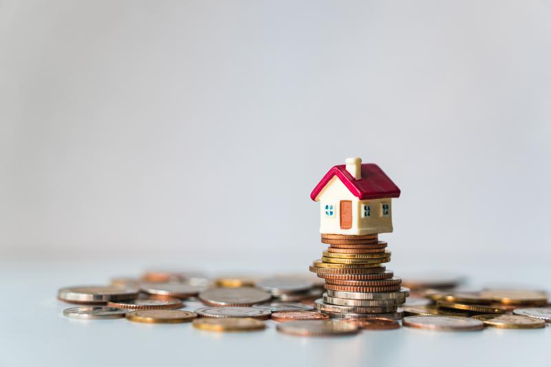 Une maison miniature au toit rouge posée sur un tas de pièces de monnaie