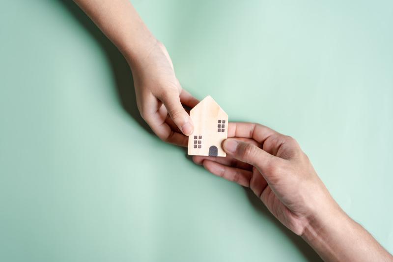 Une maison miniature en bois portée par deux mains
