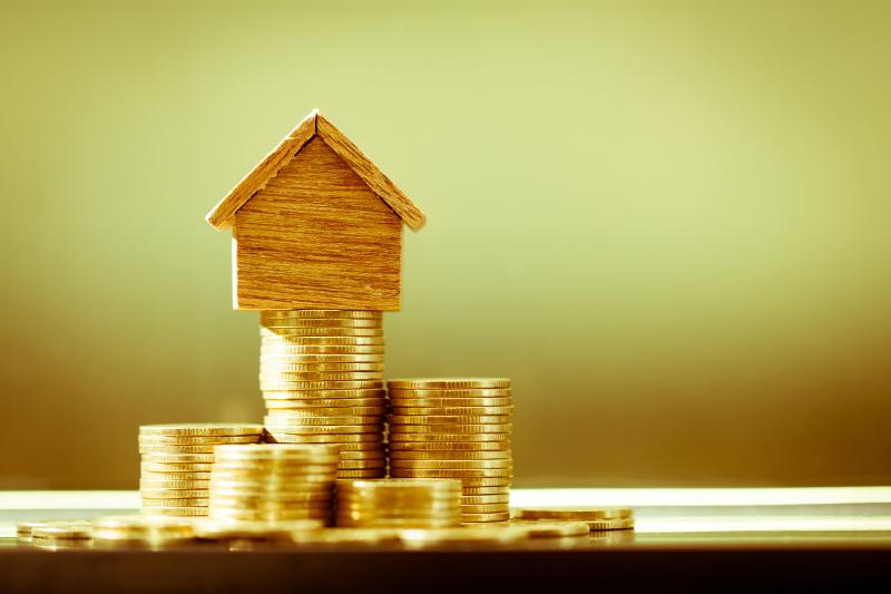 Une maison miniature en bois posée sur une pile de pièces de monnaie dorées