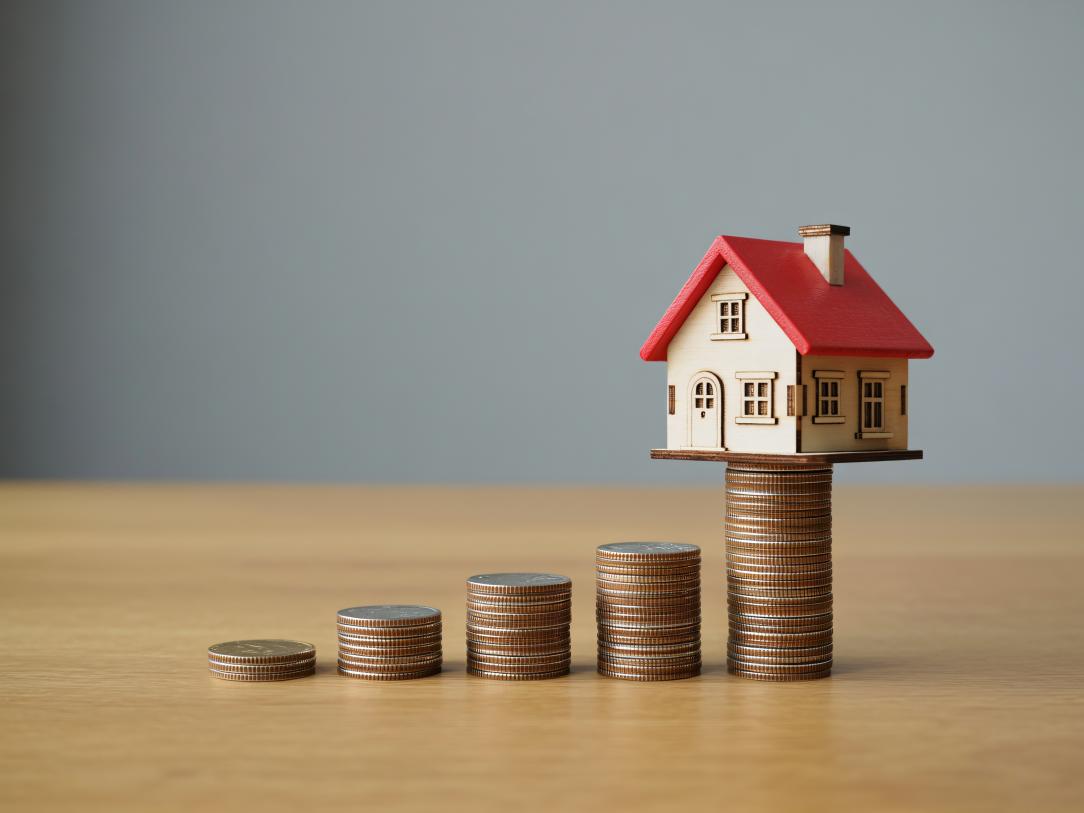 Une maison miniature posée en équilibre sur des pièces de monnaie