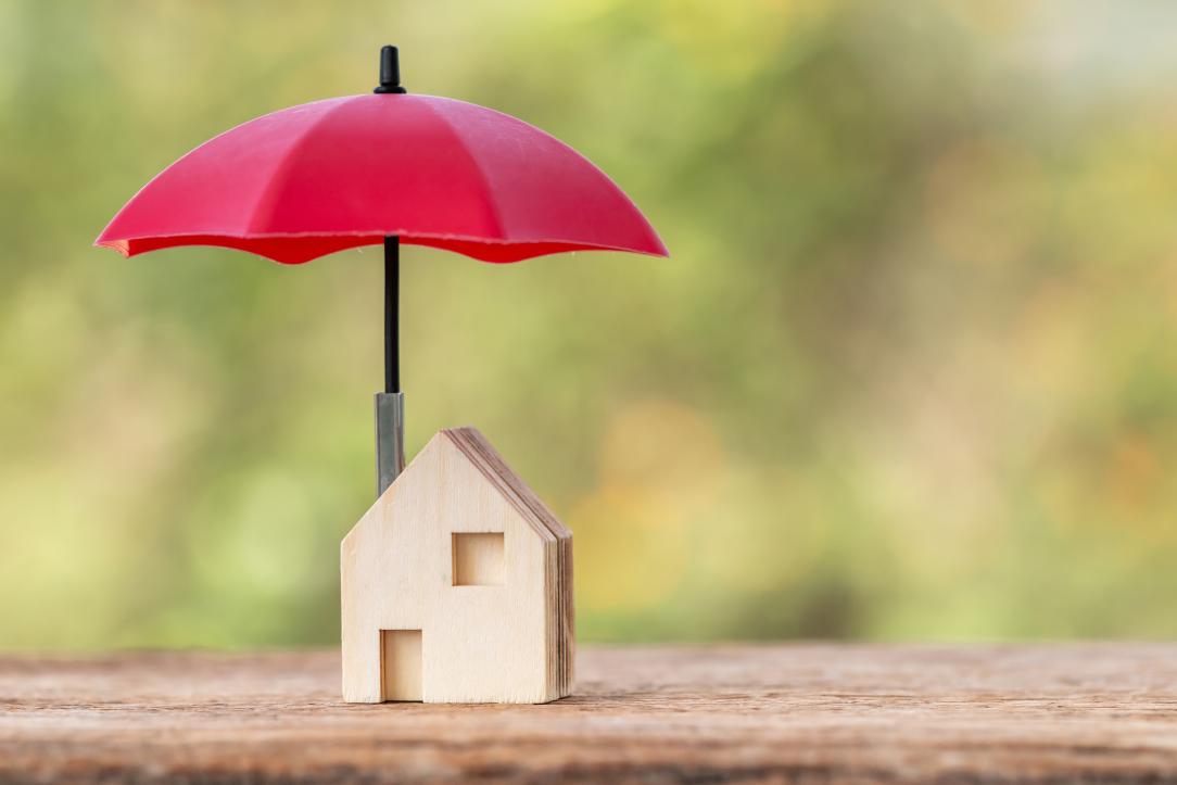Une maison miniature en bois abritée sous un parapluie rouge