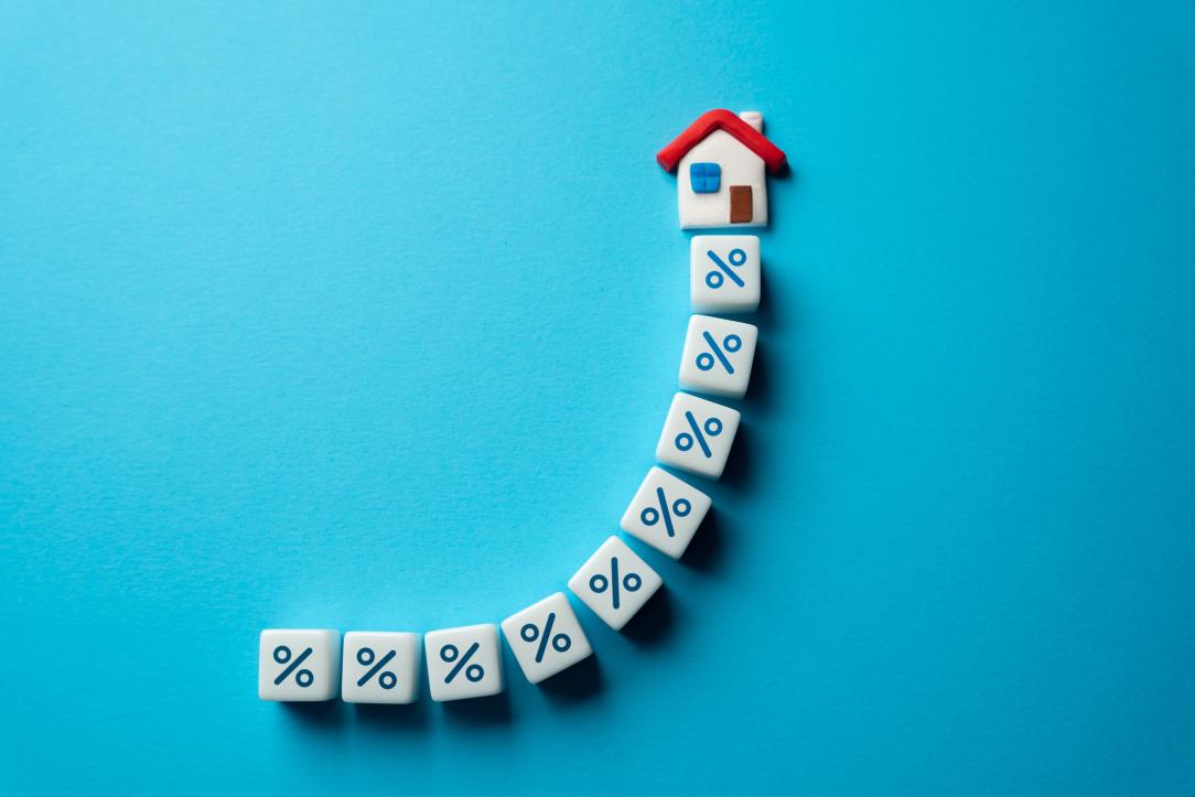 Des dés en forme de pourcentage alignés en courbe vers une petite maison, sur fond bleu turquoise
