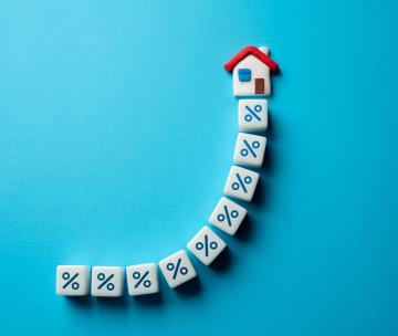 Des dés en forme de pourcentage alignés en courbe vers une petite maison, sur fond bleu turquoise
